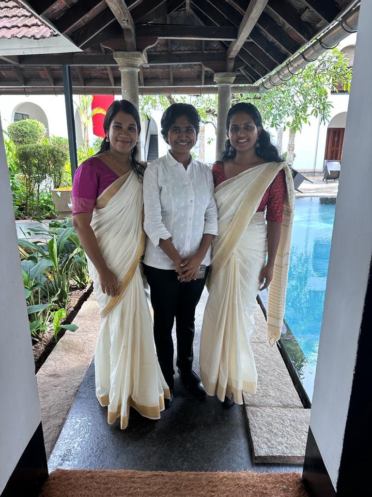 Three women standing by a pool in traditional Kerala attire